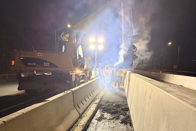 Machinery and workers install precast concrete median barrier at night