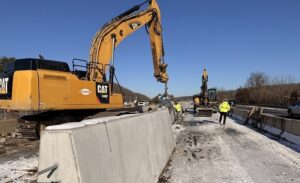 Workers assist construction in the final placement of a section of permanent concrete barrier