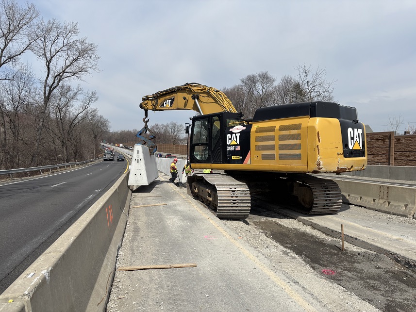 Construction equipment and workers setting a section of permanent concrete barrier in the median on Route 8