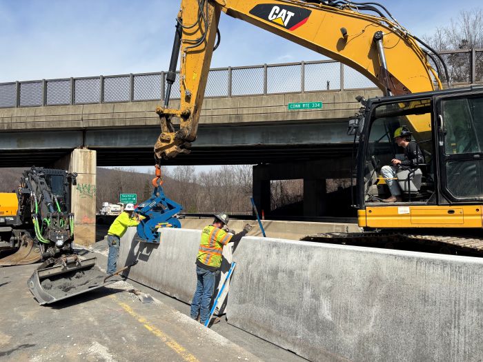 Workers assist construction in the final placement of a section of permanent concrete barrier